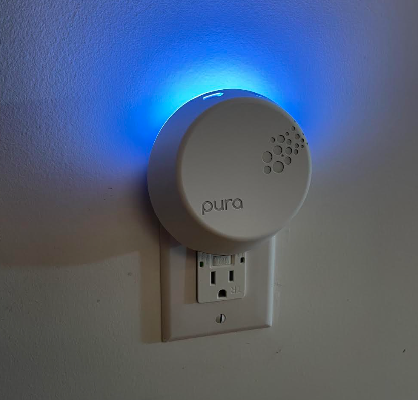 circular white Pura Smart Fragrance Diffuser with blue light plugged into socket