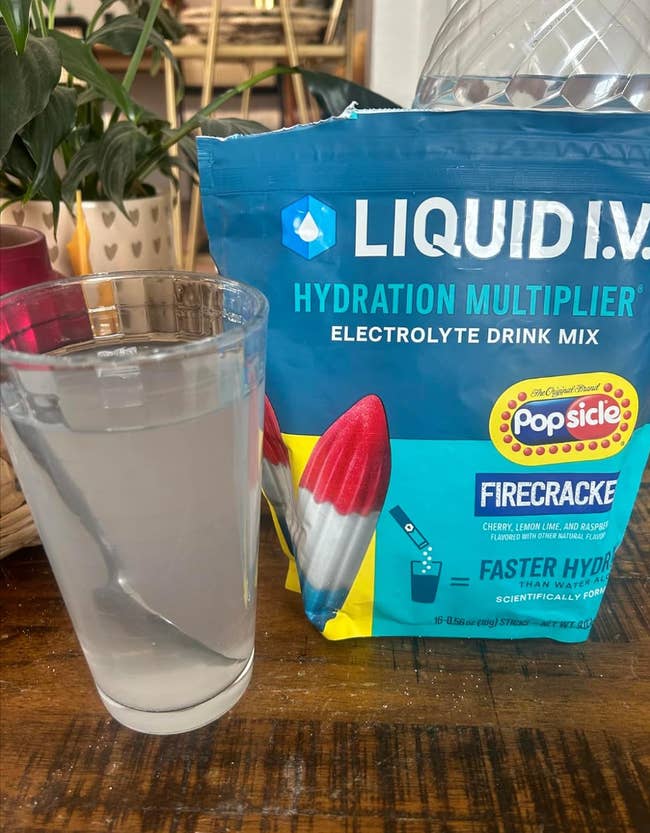 A glass of water sits beside a packet of Liquid I.V. Hydration Multiplier Electrolyte Drink Mix in Firecracker flavor