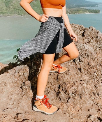 reviewer wears tan hiking boots with red laces, bike shorts, and a crop maroon top while hiking above blue lake