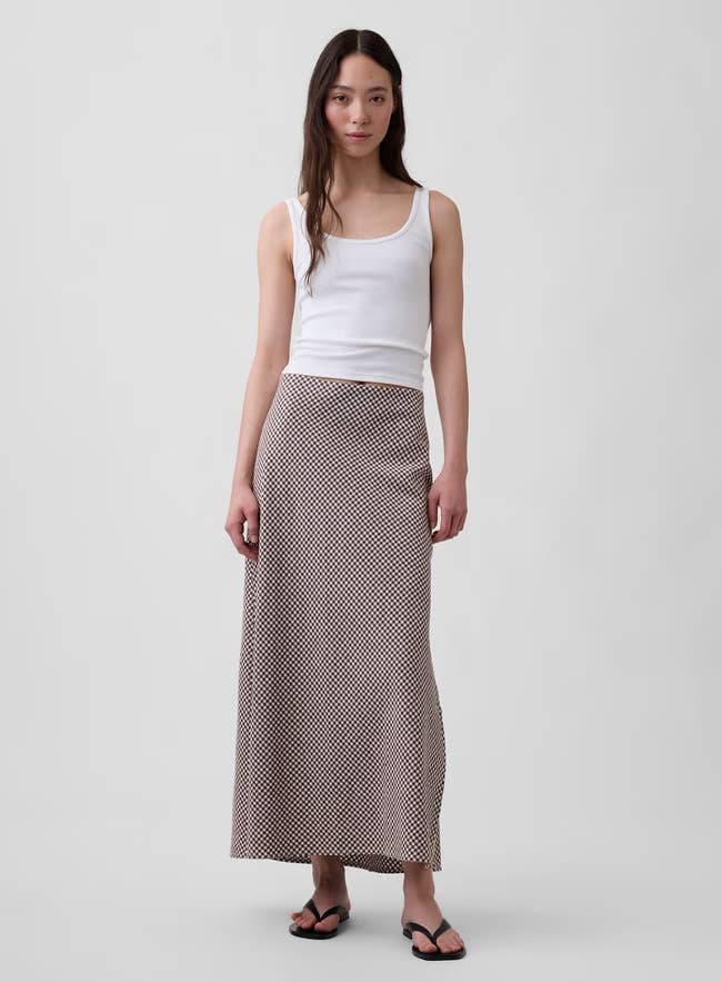 Person successful  a achromatic  vessel  top, patterned agelong  skirt, and sandals stands against a plain backdrop, modeling casual fashion