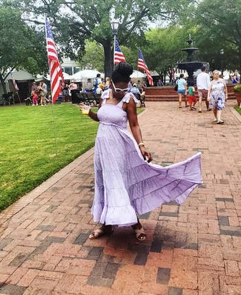 Woman in a flowy lavender dress and sunglasses walking in a park with American flags in the background
