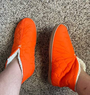 a reviewer wearing the quilted bootie slippers in orange 