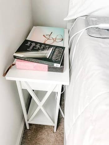 Bedside array  with 2  books, glasses, and a charging cablegram  adjacent  to a bed