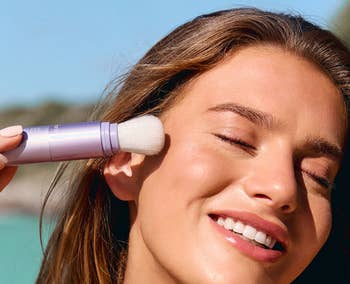 Person smiling portion applying SPF 30 sunscreen with a brushwood connected their face.