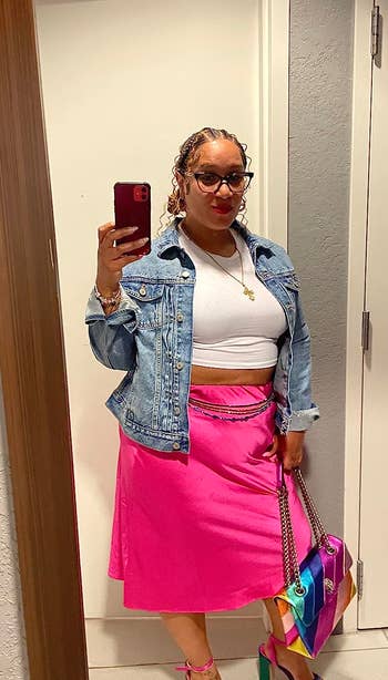 reviewer in mirror selfie with denim jacket, white top, pink skirt, multicolor bag, and sandals