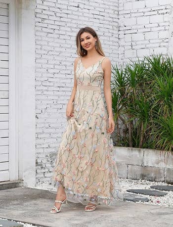Person successful  a floral sleeveless maxi formal  stands outdoors, smiling. She wears strappy sandals, suitable for a casual buying  article