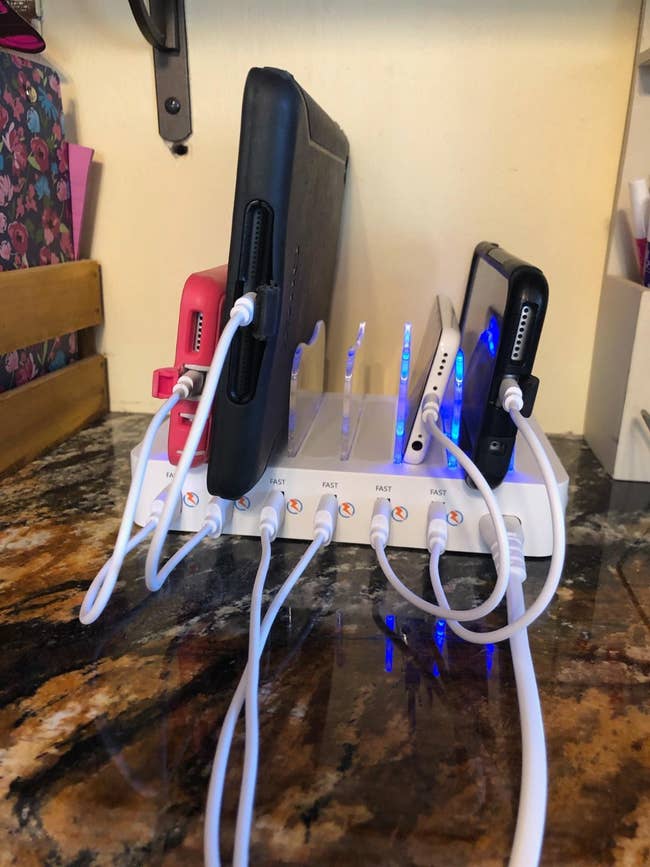 reviewer pic of the charging station from the side with some phones, a portable charger, and a Kindle plugged in