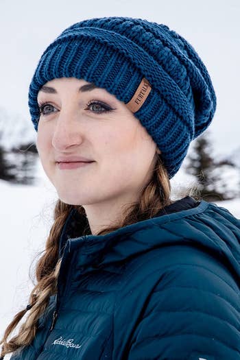 Reviewer wearing blue chunky knit beanie with blue-green puffer jacket in snow