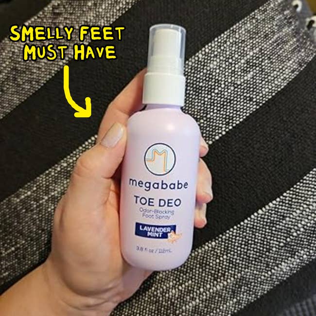 Hand holding Megababe Toe Deo ft  spray with lavender scent, captioned 