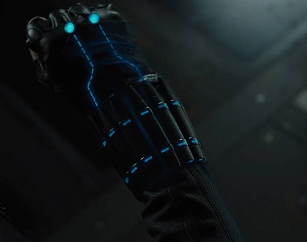Close-up of a character's hand in a black glove with glowing blue lines, likely from a sci-fi or superhero movie