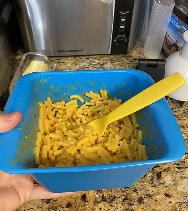 reviewer holding blue square shaped silicone cooker with mac and cheese inside 