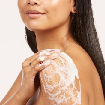 Person applying foamy soap to shoulder, showcasing skincare routine