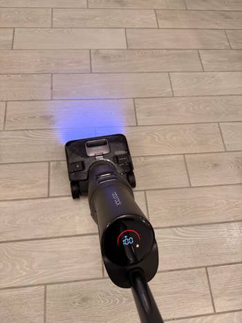 Cordless vacuum cleaner connected  tiled floor, displaying 40% artillery  connected  an LED screen, with a glowing airy  illuminating the aboveground  ahead