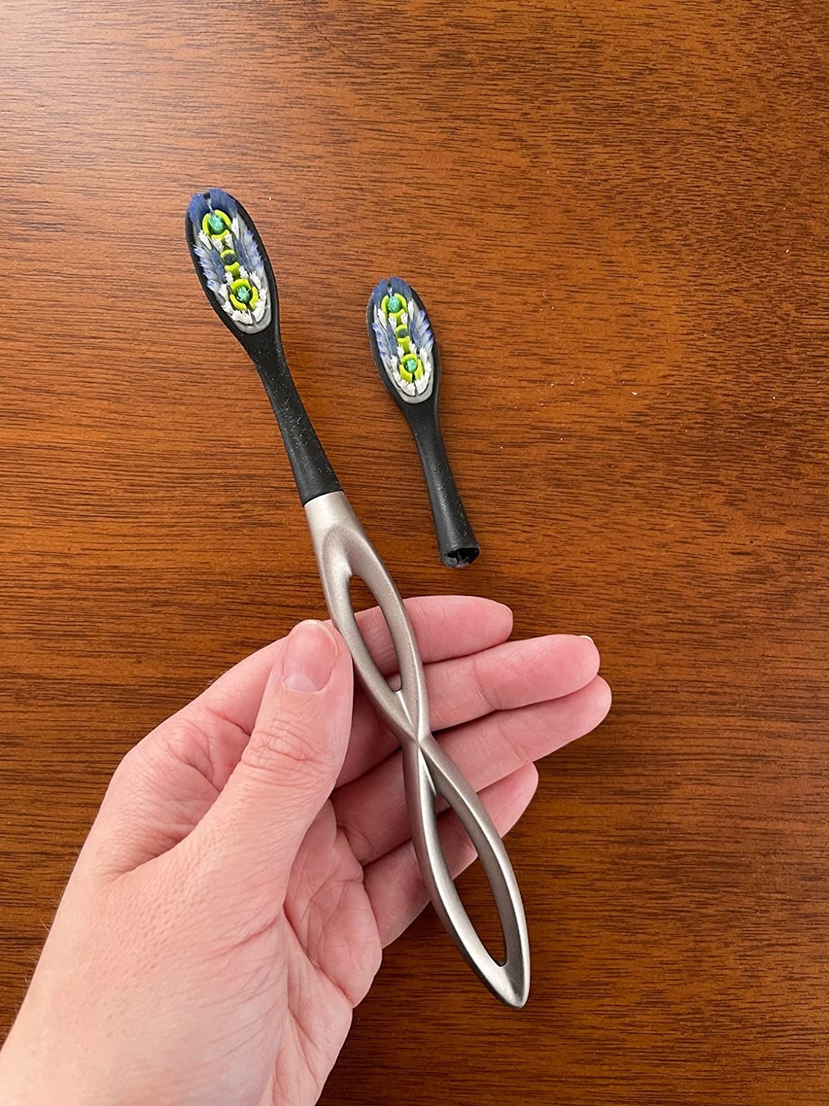 reviewer holding the silver and black toothbrush with curved handle that kind of looks like a squashed infinity symbol, next to the extra head