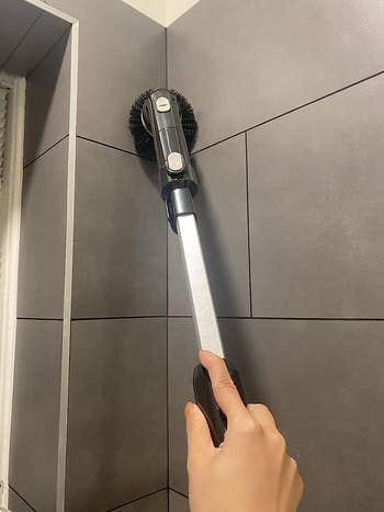 reviewer using the power scrubber to clean their shower walls