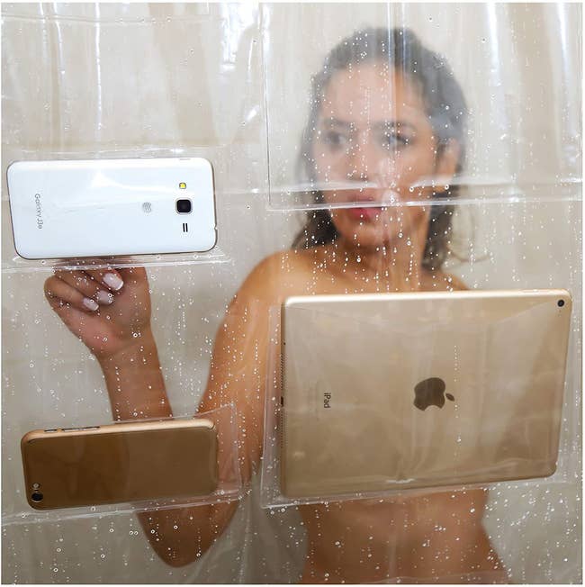 a model in the shower tapping on a phone that sits in one of the pockets of the shower liner
