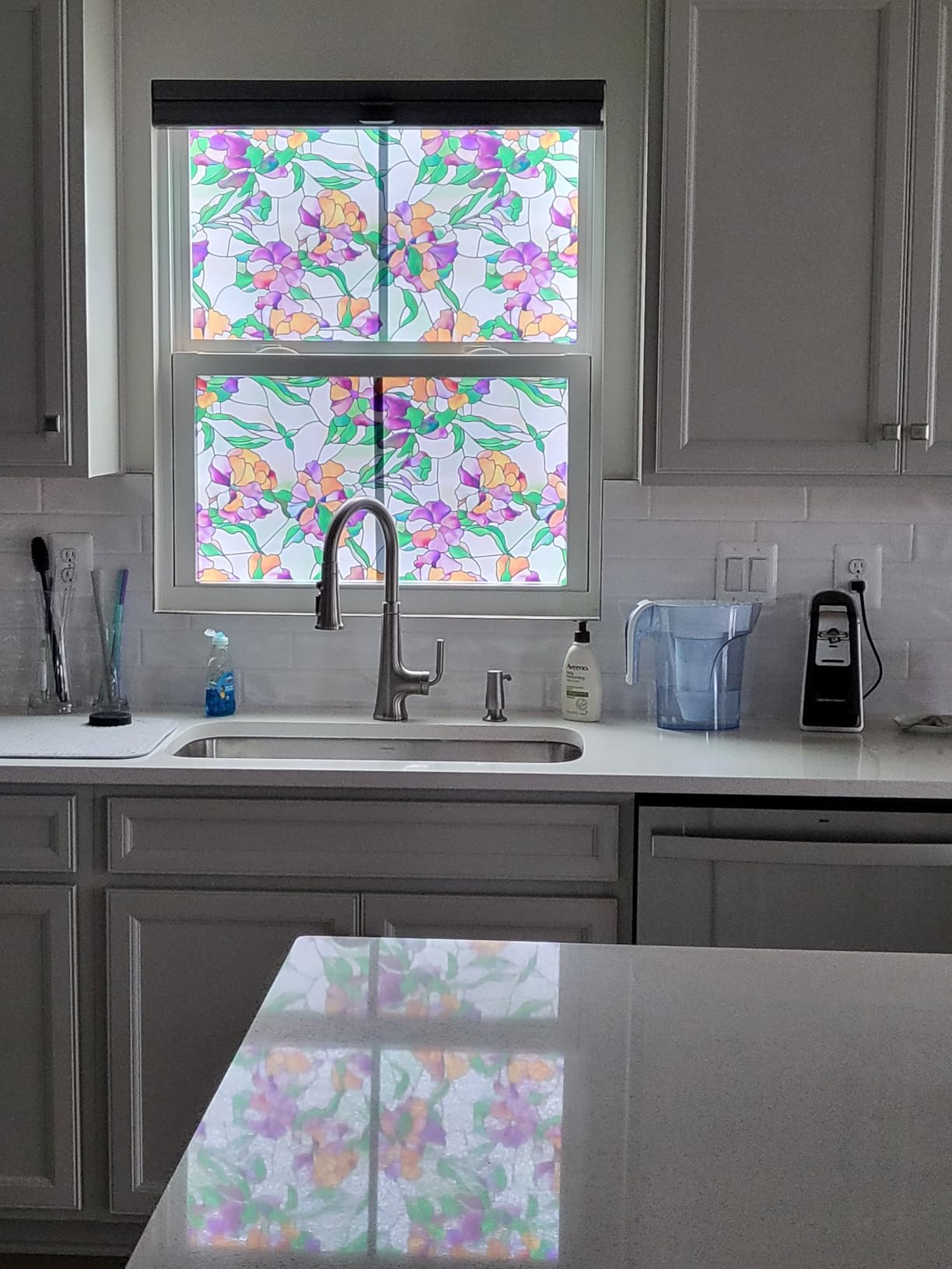 Kitchen with a modern   faucet, countertop, and appliances. Window features floral-patterned film, adding decorative privacy