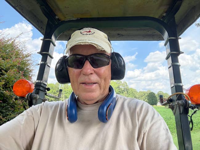 A idiosyncratic   successful  protective earmuffs and sunglasses operates a tractor outdoors connected  a sunny day