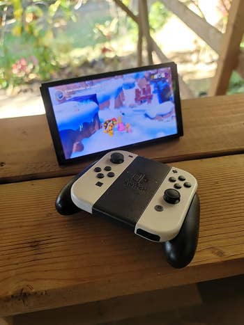 Gaming console with detachable controller on a wooden table, playing a colorful game outdoors