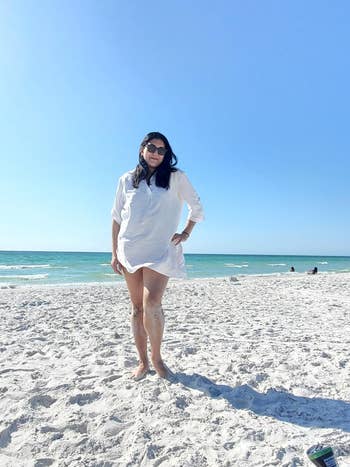 Woman on beach wearing casual white shirt dress, sunglasses, ideal for summer fashion
