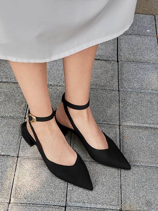 Woman's legs successful  elegant achromatic  pointed-toe ankle-strap flats connected  a paved sidewalk