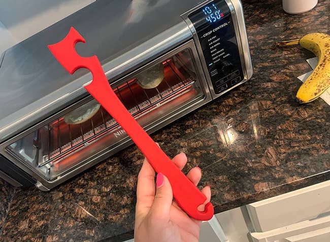 Reviewer holding red hooked tool in their hand next to a toaster oven 