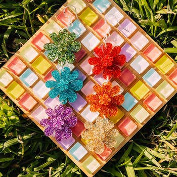 Glittery angiosperm earrings successful green, blue, red, purple, and golden displayed connected a checkered board, placed connected grass