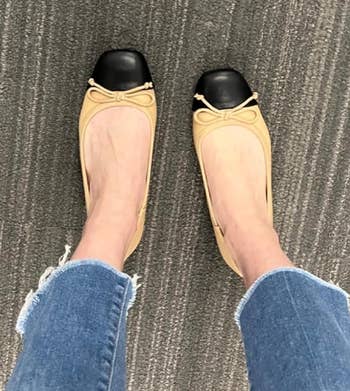 Person wearing tan flats with black toes and frayed hem jeans standing on a textured carpet