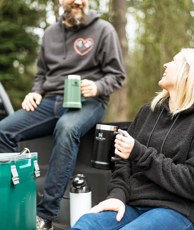 Two people smiling and celebrating with insulated drinkware in an outdoor setting