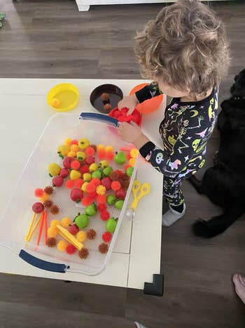 Child successful  pajamas engaged successful  sensory play   with textured balls and artifact  fruits connected  a tabletop