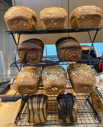 several loaves of bread cooling on four tiered stacked rack 