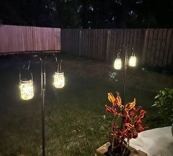 a reviewer photo of the lanterns hanging from hooks on stakes in a backyard 