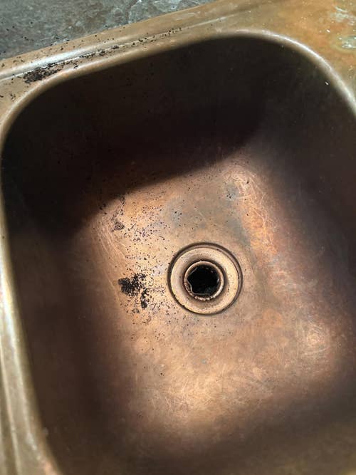 A copper sink with coffee grounds scattered around the drain