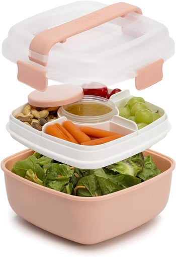 Stacked bento lunch box with compartments containing vegetables, nuts, grapes, and dip