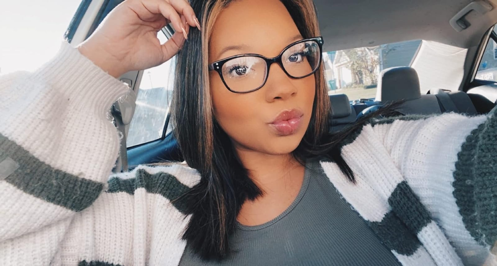 Person successful  a car   wearing glasses and a striped sweater, puckering lips for a selfie