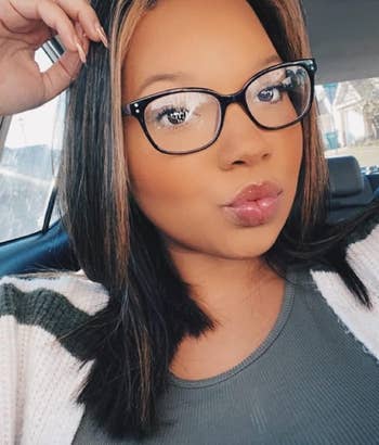 Person in a car wearing glasses and a striped sweater, puckering lips for a selfie