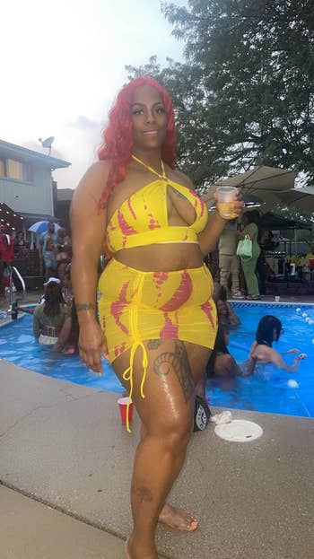 Person in a two-piece yellow swimwear with cut-out details, holding a beverage, at a poolside gathering