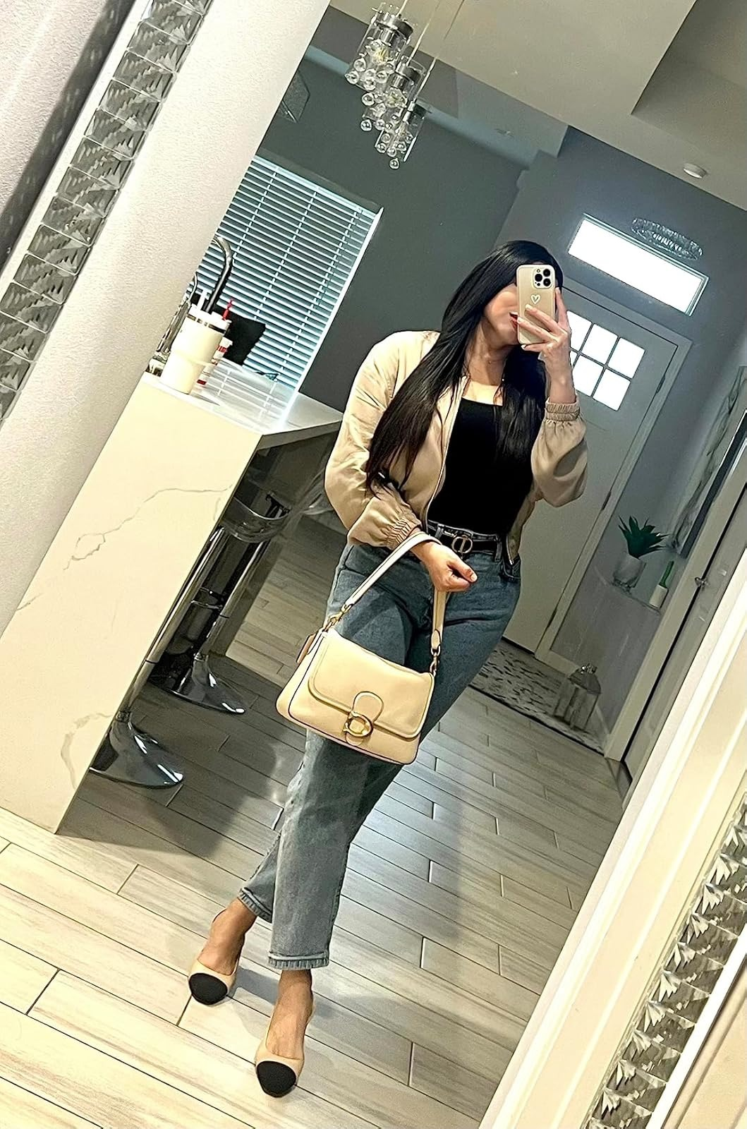 Reviewer taking a mirror selfie wearing a beige jacket, black top, blue jeans, black and beige heels while holding a beige handbag