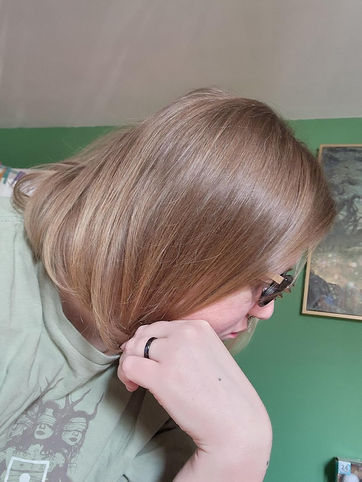 Person with chin-length hairsbreadth  and glasses successful  profile, wearing a casual greenish  graphic t-shirt and a ring, sitting successful  a country   with art