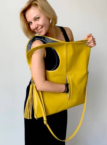 A model wearing the bag over their shoulder with their hand in a pocket and a crossbody strap attached