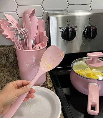 reviewer holding a pink spatula in front of the rest of the pink utensils in their holder