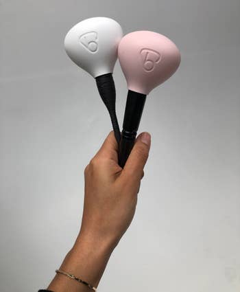 reviewer holding two makeup brushes protected by the pink and white bubble covers