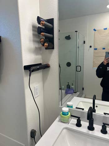 A bath  antagonistic  setup features a Dyson Airwrap and its accessories, a hairsbreadth  dryer, and a acceptable   of idiosyncratic   attraction   products adjacent  to a sink. A person's limb  is disposable   holding up   a phone, capturing the photo