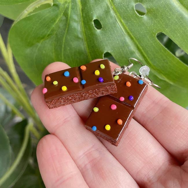 Model holding two earrings that look like brownies with multicolored sprinkles on them 