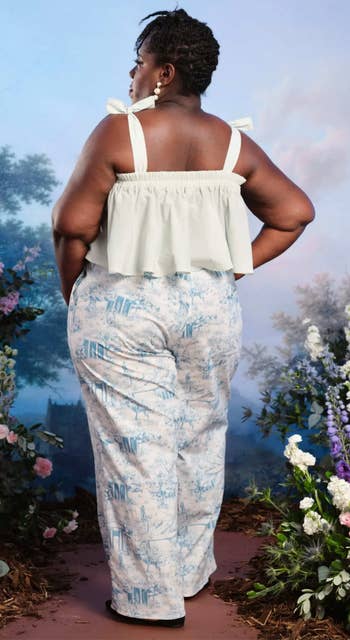 model standing in a garden wearing high-waisted printed trousers and a ruffled off-the-shoulder top