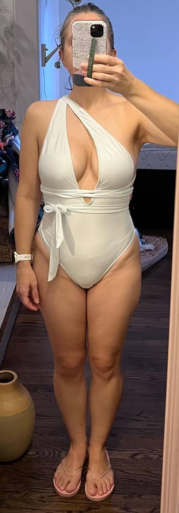 Person taking a mirror selfie wearing a stylish, one-piece swimsuit with cut-out details, suitable for a fashion or shopping article