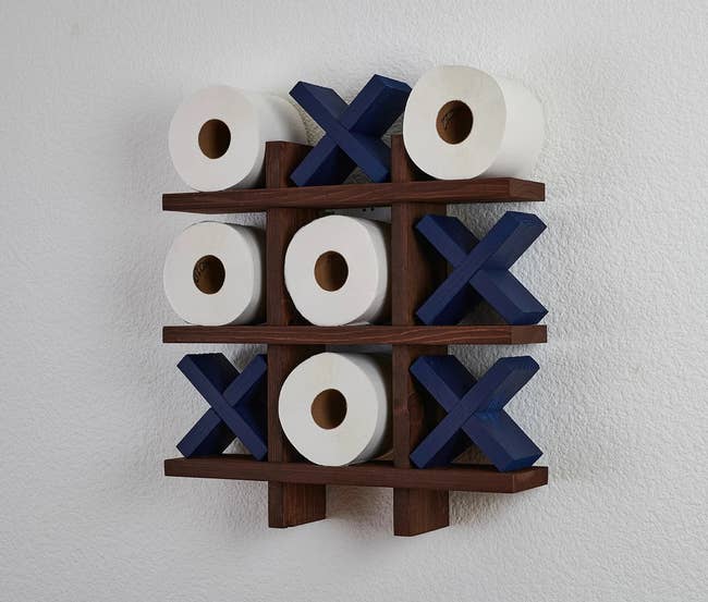 the wall-mounted wooden tic tac toe board with blue exes and five rolls of toilet paper