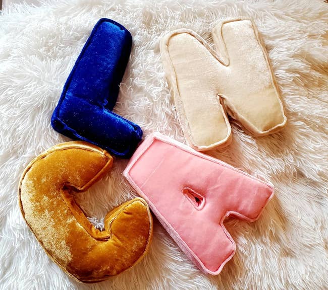 Four pillows shaped like letters: a blue L, an ivory N, a pink A, and a gold C