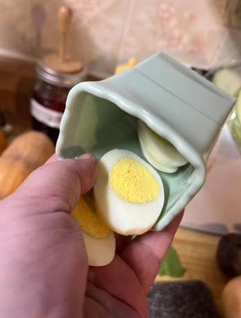 A hand holding a green cup with a hard-boiled egg sliced in several pieces
