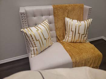 reviewer's white chair with two throw pillows with the white and gold pillow cases on them